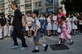 中国・香港の学校で、警察によって胸を撃たれた高校生の同級生らが抗議のために集まる中、子どもを連れて歩く保護者ら（2019年10月2日撮影）。(c)Mohd RASFAN / AFP