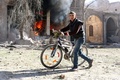 空爆を受けたとされるシリア・アレッポの反体制派支配地域バーブ・ナイラブで、炎上する家の前を自転車を押しながら横切る若者（2016年11月19日撮影）。(c)AFP/AMEER ALHALBI
