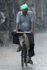 インドのアムリトサル（Amritsar）で、豪雨の中を自転車で移動する男性（2013年8月12日撮影）。(c)AFP/NARINDER NANU