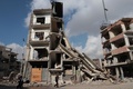 シリアの首都ダマスカス東郊にある反体制派が掌握するドゥーマ地区で、停戦が発効した初日、破壊された建物のそばを歩く人々（2016年12月30日撮影）。(c)AFP/Abd Doumany