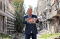 シリアの首都ダマスカスのパレスチナ難民キャンプで、同地で10年前に撮影されたアトリエで作業する自身の写真を手にするパレスチナ人画家のモハメド・ラクイアさん（70）。アトリエは破壊され、作品は持ち去られたという（2021年3月7日撮影）。(c)Maher AL MOUNES / AFP