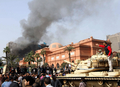 エジプトの首都カイロ（Cairo）で、放火され炎上する与党・国民民主党本部（奥）と、エジプト考古学博物館（Egyptian Museum、手前）を取り囲んで守る人々と戦車（2011年1月30日撮影）。(c)AFP/MARCO LONGARI