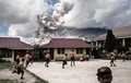 インドネシアのカロで、火山灰を噴き上げるシナブン山を背にして、校舎の外で遊ぶ小学生たち（2017年2月10日撮影）。(c)AFP