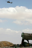パレスチナ自治区ヨルダン川西岸（West Bank）のヘブロン（Hebron）近郊で、墜落したイスラエル空軍の戦闘機の残がいを捜索する同軍のヘリコプターと、テントのかたわらに座るパレスチナ人（2009年9月13日撮影）。(c)AFP/HAZEM BADER
