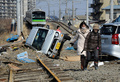 東日本大震災で線路に横倒しになった車のそばを歩く人々。宮城県多賀城市で（2011年3月13日撮影）。(c)TORU YAMANAKA / AFP