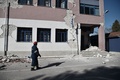 ギリシャ中部テッサリア地域のダマシ村で、地震により損壊した学校校舎のそばを歩く消防隊員（2021年3月3日撮影）。(c)Sakis MITROLIDIS / AFP