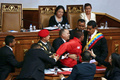 ベネズエラの首都カラカス（Caracas）で行われた大統領の就任宣誓式で、演壇でニコラス・マドゥロ（Nicolas Maduro）新大統領（右）を押しのけた赤いジャケットの男を取り押さえるディオスダド・カベジョ（Diosdado Cabello）国民議会議長（中央）と警備員の男性ら（2013年4月19日撮影）。(c)AFP/Francisco Boza