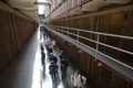 米カリフォルニア（California）州サンフランシスコ（San Francisco）にある悪名高いアルカトラズ島（Alcatraz Island）は21日、島に作られた連邦刑務所の閉鎖から50年を迎えた。アルカトラズ島は当初、軍事要塞化され、やがて軍刑務所となった。施設は1934年に連邦刑務所局（Bureau of Prisons）に移管されて連邦刑務所となった後、1963年に閉鎖された。現在は国立公園の一部となっている。

アルカトラズ島を管理する国立公園局（National Park Service）では、閉鎖50年を記念して、閉鎖される直前の刑務所を撮影した写真展を同島で開催している。写真はいずれもロサンゼルス（Los Angeles）を中心に活動していたフリーカメラマン、リー・ウィーナー（Leigh Wiener）氏が撮影したもので、新たに見つかった作品という。

写真は、旧アルカトラズ刑務所の内部を見て歩く観光客（2013年3月21日撮影）。(c)AFP/Getty Images/Justin Sullivan