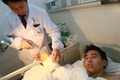 中国中部・湖南（Hunan）省長沙（Changsha）の病院で、シャオ・ウェイ（Xiao Wei）さん（ベッドで横になっている人物）のかかと付近に接続された後、腕先に再接合された手の状態を確認する医師（2013年12月10日撮影）。(c)AFP