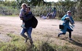 ハンガリーとセルビアの国境に設置された有刺鉄線をくぐり抜け、走り去る移民の家族（2015年8月28日撮影）。(c)AFP/ATTILA KISBENEDEK
