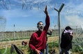 ギリシャ・イドメニの対マケドニア国境で、国境開放を求める移民らがマケドニア警察と衝突する中、破られたフェンスを越えるよう移民らに呼び掛ける男性（2016年4月10日撮影）。(c)AFP/BULENT KILIC