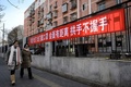 中国・北京で、人々にマスクの着用や手洗いを呼び掛ける横断幕の前を、マスクをして歩く人々（2020年2月1日撮影）。(c)NOEL CELIS / AFP