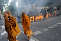 タイの首都バンコク（Bangkok）で、デモ隊が炎上させたバスの前を歩く僧侶（2009年4月13日撮影）。(c)AFP/PORNCHAI KITTIWONGSAKUL