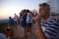 イスラエル南部スデロット（Sderot）で、パレスチナ自治区ガザ地区（Gaza Strip）を見下ろす丘の上に集まり、空爆やロケット弾による双方の攻撃の様子を見るイスラエル人たち（2014年7月9日撮影）。(c)AFP/MENAHEM KAHANA