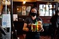 英ロンドン・ストラットフォードにあるパブで、マスク姿でビールを運ぶ従業員（2020年7月4日撮影）。(c)Tolga Akmen / AFP
