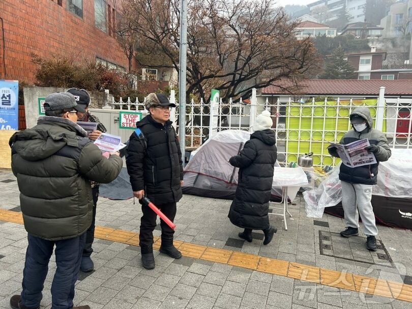 14日、弾劾反対集会で配布された新聞形式のビラを読む参加者ら(c)news1