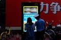 中国の上海市街で、交差点で信号無視をした人たちを顔認証技術で特定するシステムについて説明する警察官（2017年8月9日撮影）。(c)AFP/CHANDAN KHANNA 