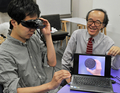 都内の研究室で、ビスケットを実際よりも大きく見せるゴーグルについて説明する東京大学（University of Tokyo）の廣瀬通孝（Michitaka Hirose）教授（右、2012年6月2日撮影）。(c)AFP/Yoshikazu TSUNO
