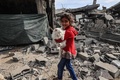 パレスチナ自治区ガザ地区ラファで、イスラエル軍の爆撃を受けた建物のそばを猫を抱いて歩く子ども（2024年2月12日撮影）。(c)SAID KHATIB / AFP