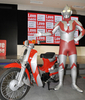 東京・青山にあるホンダ（Honda Motor）のショールームで始まった原付バイク「スーパーカブ（Super Cub）」の著名人デザイン展で、ウルトラマン・デザインのスーパーカブと並ぶウルトラマン（2010年2月12日撮影）。(c)AFP/Yoshikazu TSUNO