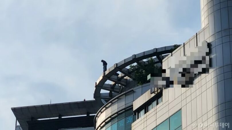 投身騒動が発生したソウル・江南駅近くの高層ビル屋上で、男性が身を乗り出している様子(c)MONEYTODAY