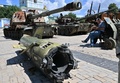 ウクライナの首都キーウで、聖ミハイル黄金ドーム修道院前に展示されたロシア軍の兵器に腰掛け本を読む人（2022年7月26日撮影）。(c)Sergei SUPINSKY / AFP