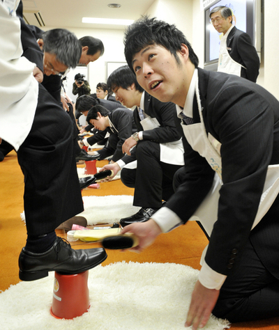 靴クリームメーカーの入社式、新入社員が先輩の靴磨き