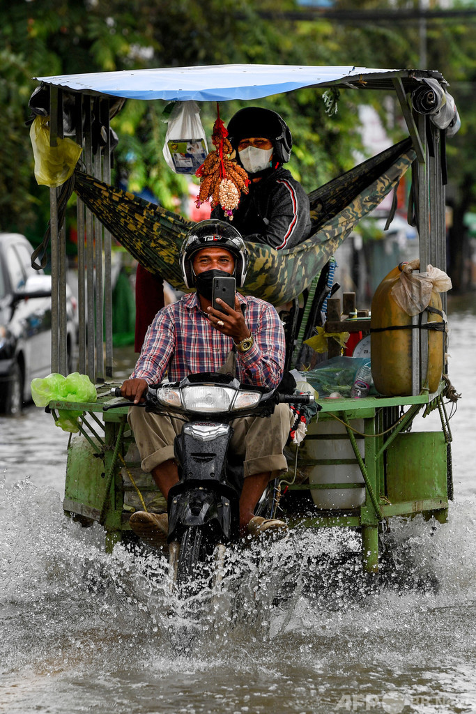 【今日の1枚】水しぶきもへっちゃら？ 冠水した通りを進む二輪車、カンボジア
