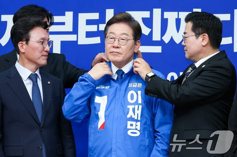 4月28日、ソウル・汝矣島の国会で開かれた最高委員会で、共に民主党のパク・チャンデ代表職務代行兼院内代表がイ・ジェミョン（李在明）大統領候補に選挙用の上着を着せ、襟元を整えている(c)news1