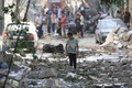 イスラエル軍による人質救出作戦で損傷した建物と散乱したがれきの中を移動する子ども。パレスチナ自治区ガザ地区中部ヌセイラット避難民キャンプで（2024年6月9日撮影）。(c)EYAD BABA / AFP