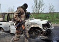 銃撃戦が起きたウクライナ東部スラビャンスク（Slavyansk）近郊の検問所で、焼け焦げた車両の横を通る武装した親ロシア派の男性（2014年4月20日撮影）。(c)AFP/GENYA SAVILOV