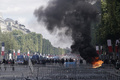 フランス・パリで、フランス革命記念日の軍事パレードが行われた後、シャンゼリゼ通りでの抗議デモの放火で上がった炎の前を通る憲兵隊ら（2019年7月14日撮影）。(c)Abdulmonam EASSA / AFP