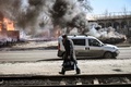 ウクライナ北東部ハリコフで、砲撃を受け炎上した車のそばを通り避難する人（2022年3月25日撮影）。(c)Aris Messinis / AFP