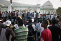 ハイチの首都ポルトープランス（Port-au-Prince）で、崩壊した大統領官邸のフェンスの内側に姿を現したルネ・プレバル（Rene Preval）ハイチ大統領を見ようと集まった市民（2010年1月30日撮影）。(c)AFP/JEAN-PHILIPPE KSIAZEK