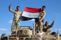 イラクのアンバル州ヒートから数キロ北のモハマディ村で軍用車両の上でイラク国旗を広げる政府の治安部隊員ら（2016年3月18日撮影）。(c)AFP/MOADH AL-DULAIMI