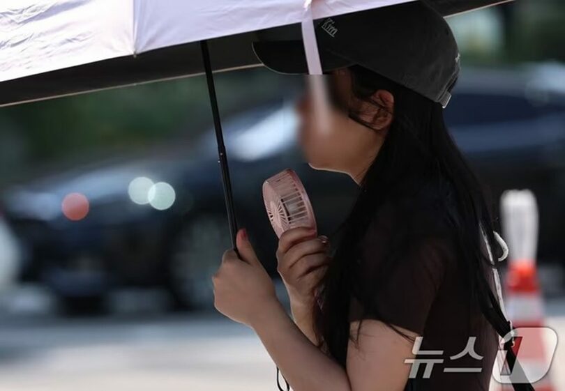 ソウル・光化門交差点で、日傘と携帯扇風機を使って暑さをしのぐ市民(c)news1